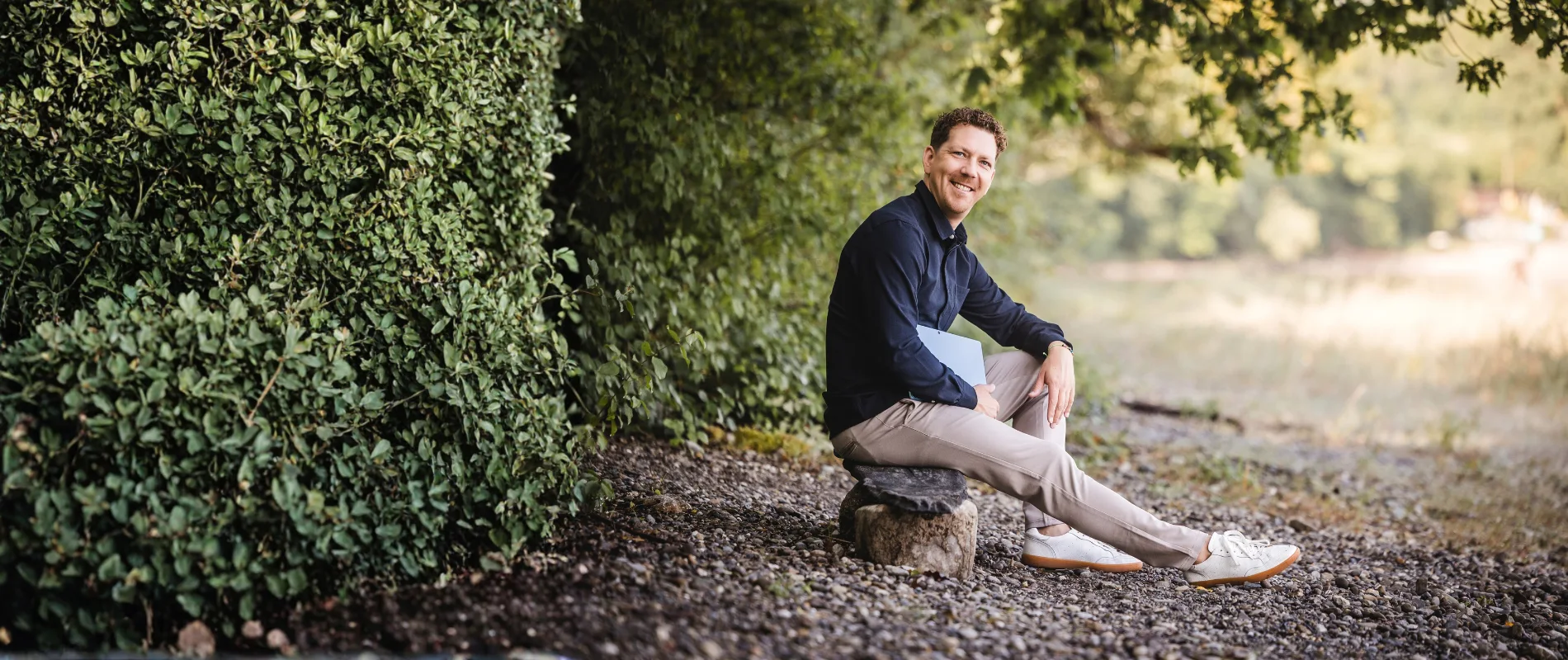 Michael Thiess sitzt mit Unterlagen am Rand eines Waldwegs
