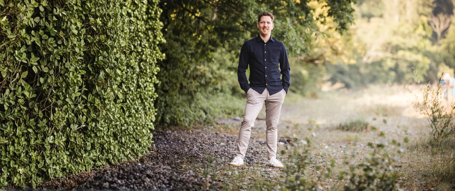 Michael Thiess steht in einer natürlichen Parklandschaft und blickt freundlich in die Kamera