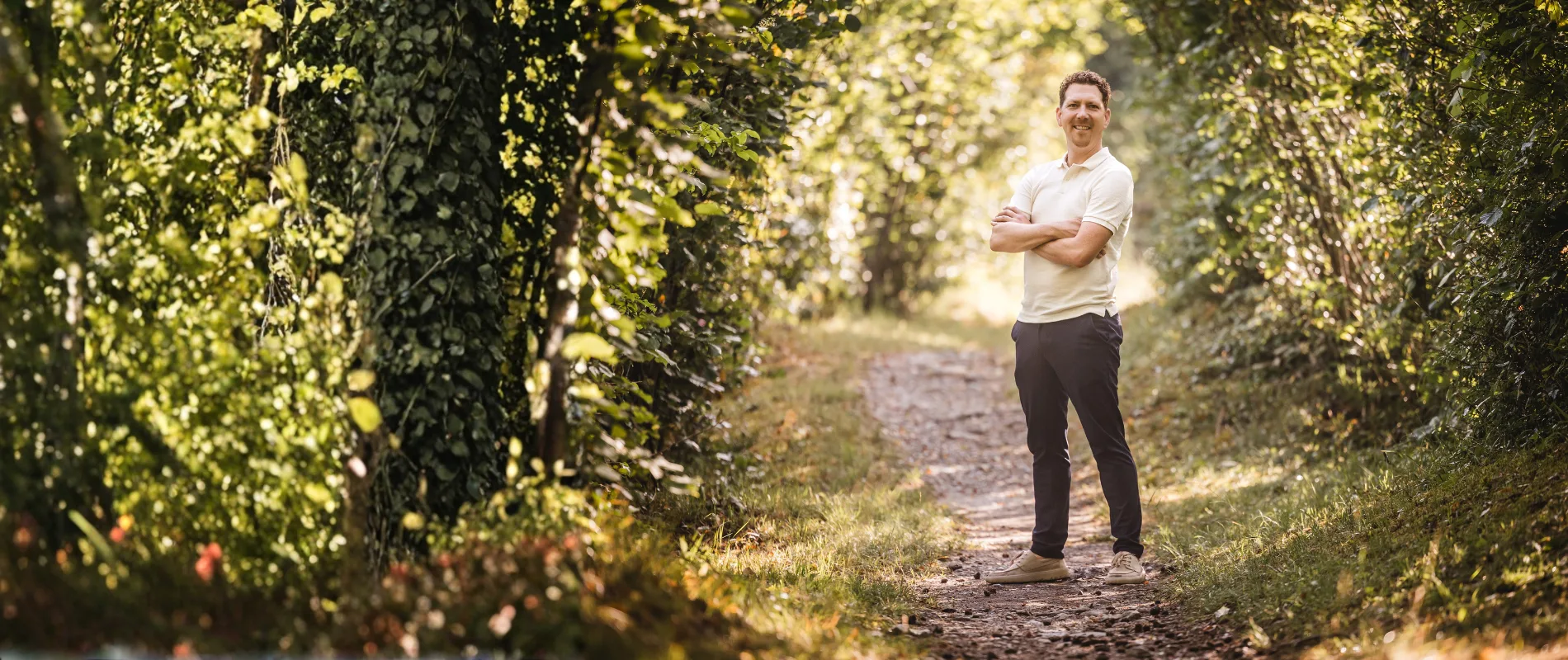 Michael Thiess steht auf einem sonnigen Waldweg